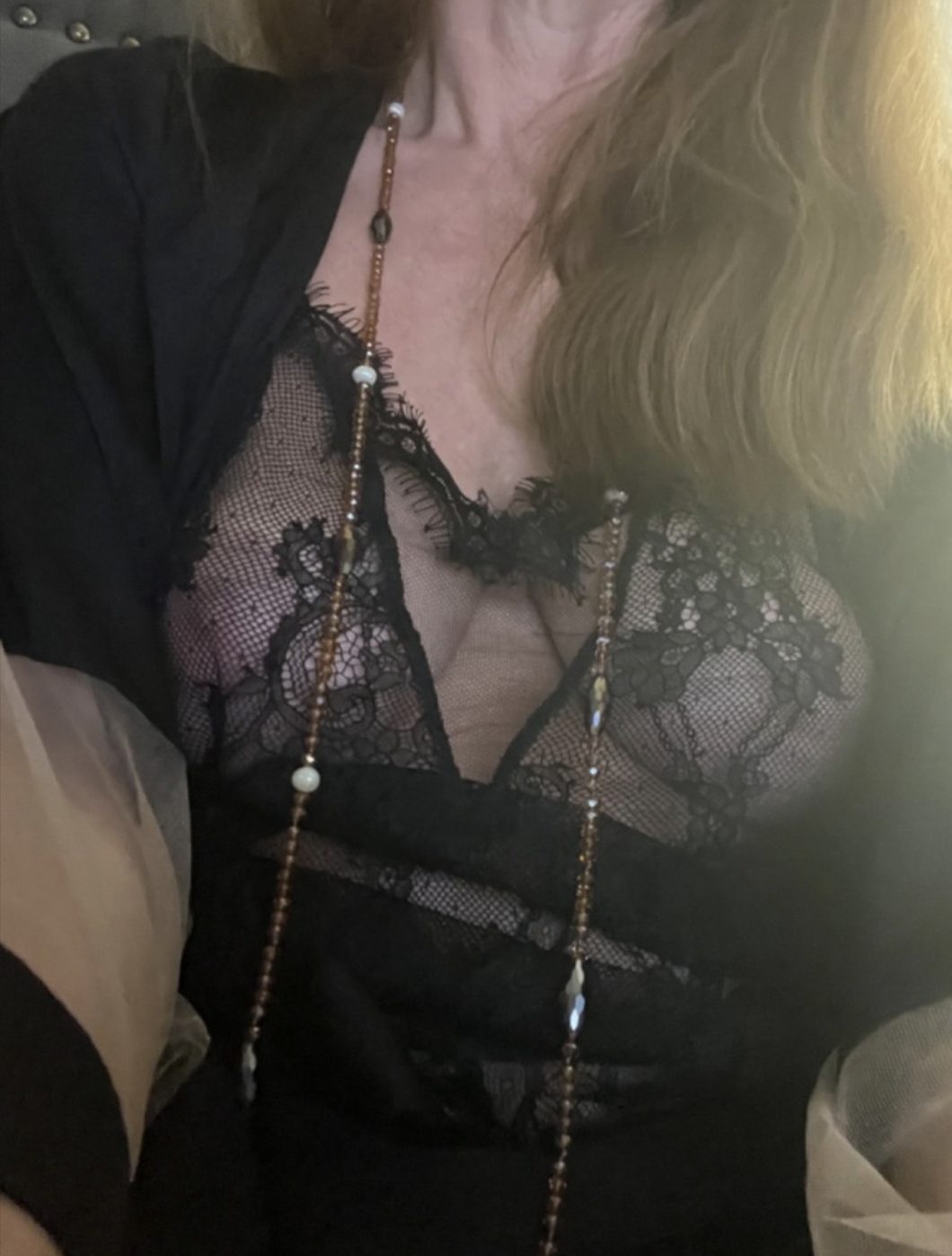 Rose en body de dentelle noire, un long sautoir de perles sur la poitrine.